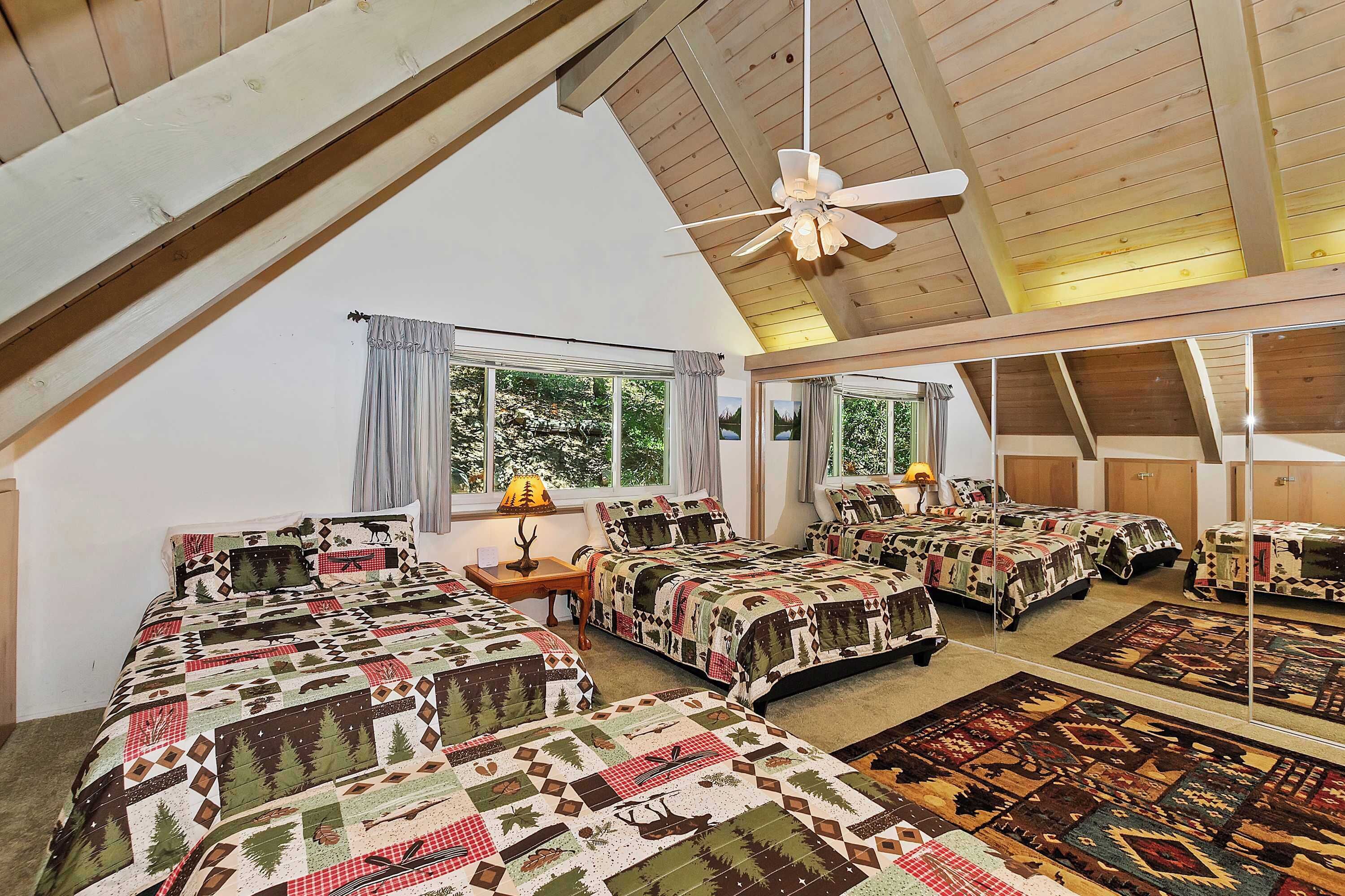 A spacious attic bedroom with multiple beds, large windows, and a ceiling fan.