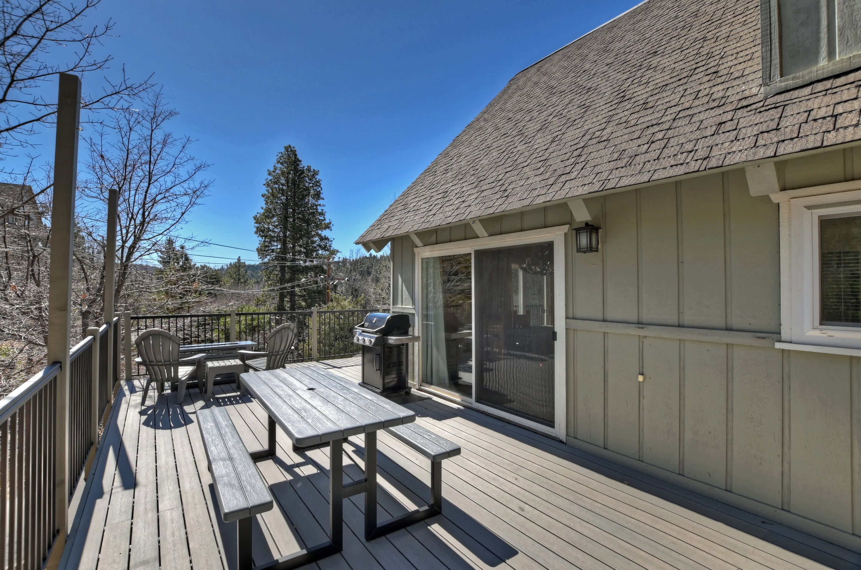 Une terrasse en bois avec une table et des chaises, un barbecue et une porte-fenêtre coulissante donnant sur un espace abrité.