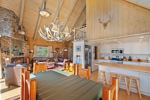 A spacious living area with a fireplace, a dining table with wooden chairs, and a kitchen with white cabinets and stainless steel appliances.