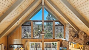 Une pièce aux hauts plafonds, avec des poutres en bois, de grandes fenêtres, une cheminée en pierre et un lustre.