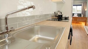 A modern kitchen with a stainless steel sink, a wooden countertop, and a view of a bedroom with a bed and a window.