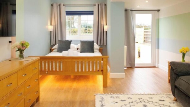 A bedroom with a bed, wooden dresser, and a view of the outdoors.