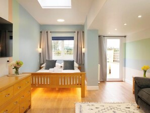 A bedroom with a bed, wooden dresser, and a view of the outdoors. - Light Spacious Studio Apartment with Terrace (Guernsey)