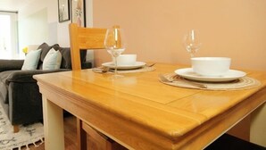 A dining table set with white plates, bowls, and wine glasses, with a wooden chair and a sofa in the background.