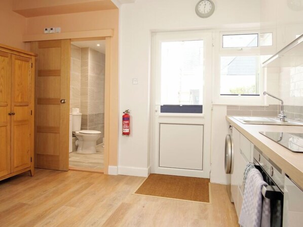 A modern kitchen with wooden cabinets, a built-in oven, and a window above the sink. - Light Spacious Studio Apartment with Terrace (Guernsey)