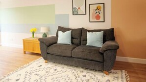 A living room with a grey sofa, a wooden side table, a white rug, and two framed artworks on the wall.