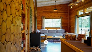A cozy cabin interior with a stone wall, a fireplace, a sofa, and a dining area. - Cabana Fruta Fina - Urubici - SC (Urubici)