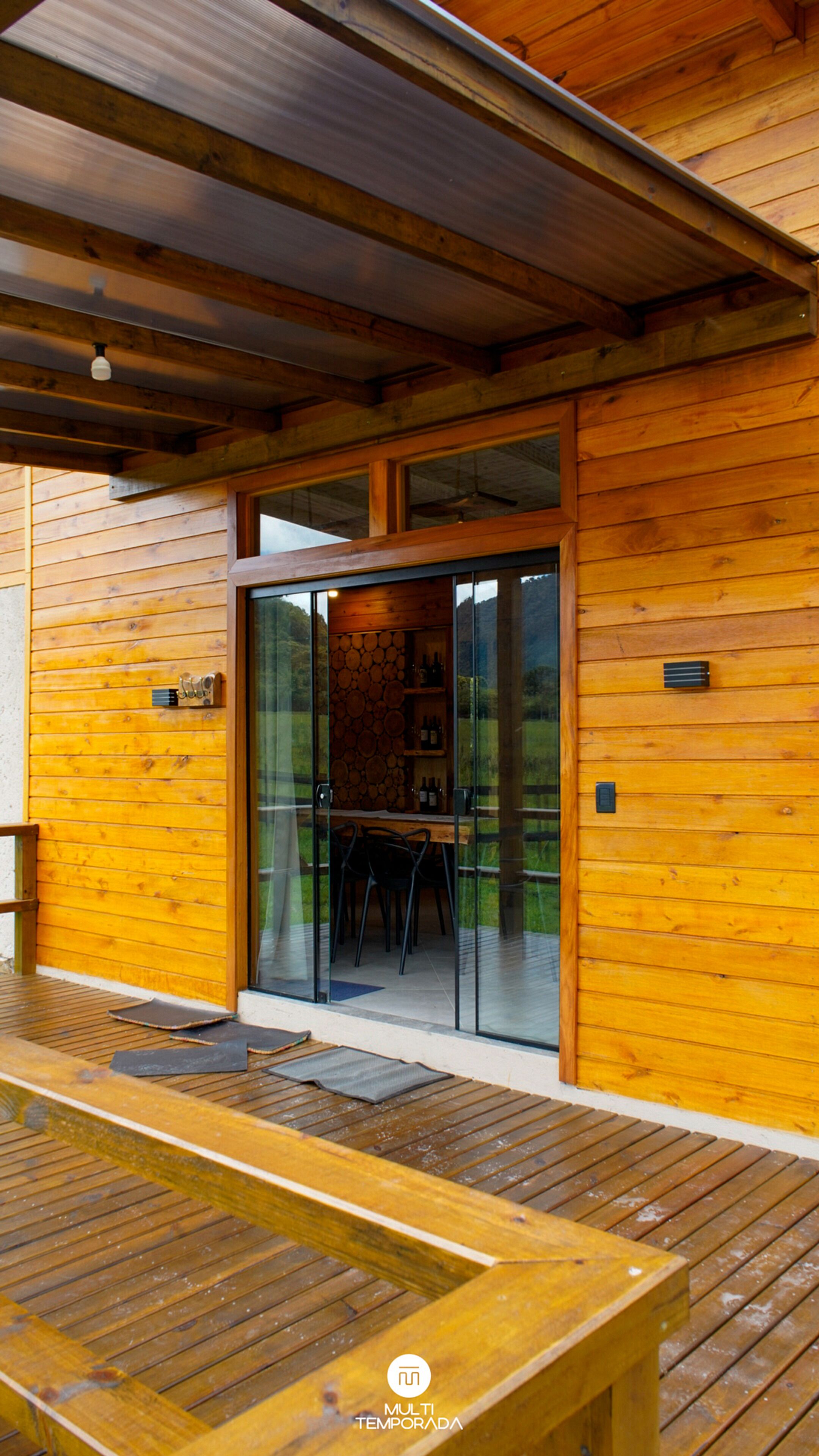 Uma cabana de madeira com porta de vidro que dá para o interior, incluindo sala de jantar com cadeiras e mesa.