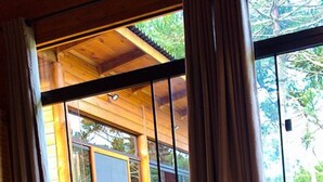 A wooden cabin room with a bed, large windows, and a view of the outdoors. - Cabana Fruta Fina - Urubici - SC (Urubici)