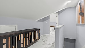 A hallway with a dark wooden console, a white door, and a staircase leading to a bedroom with a white bed.