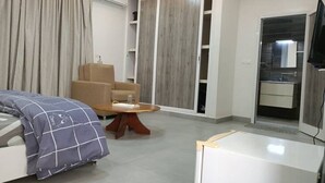 A modern hotel room with a bed, a chair, a small table, a TV, and a wardrobe.