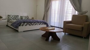 A bedroom with a bed, a chair, a small table, and a window with curtains.