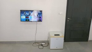 A room with a mounted television displaying a streaming service interface, a white device on the floor, and a closed door.