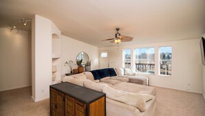 A spacious living room with a large beige sectional sofa, a ceiling fan, and a view of a building through large windows.
