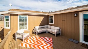 A wooden deck with a white sofa and a white chair, a chevron-patterned rug, and a satellite dish.