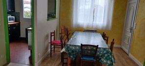 A dining area with a table set for four, surrounded by chairs, a window with curtains, and a view of the outside. - Family home for 10 people, 600 m from the ocean – large garden (Mimizan)