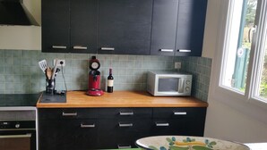 A kitchen with dark cabinets, a microwave, a red blender, and a clock. - Family home for 10 people, 600 m from the ocean – large garden (Mimizan)