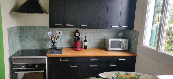 Una cocina con gabinetes oscuros, un microondas, una licuadora roja y un reloj.