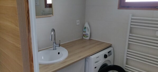 A compact bathroom with a wooden countertop, a white sink, a washing machine, and a radiator.