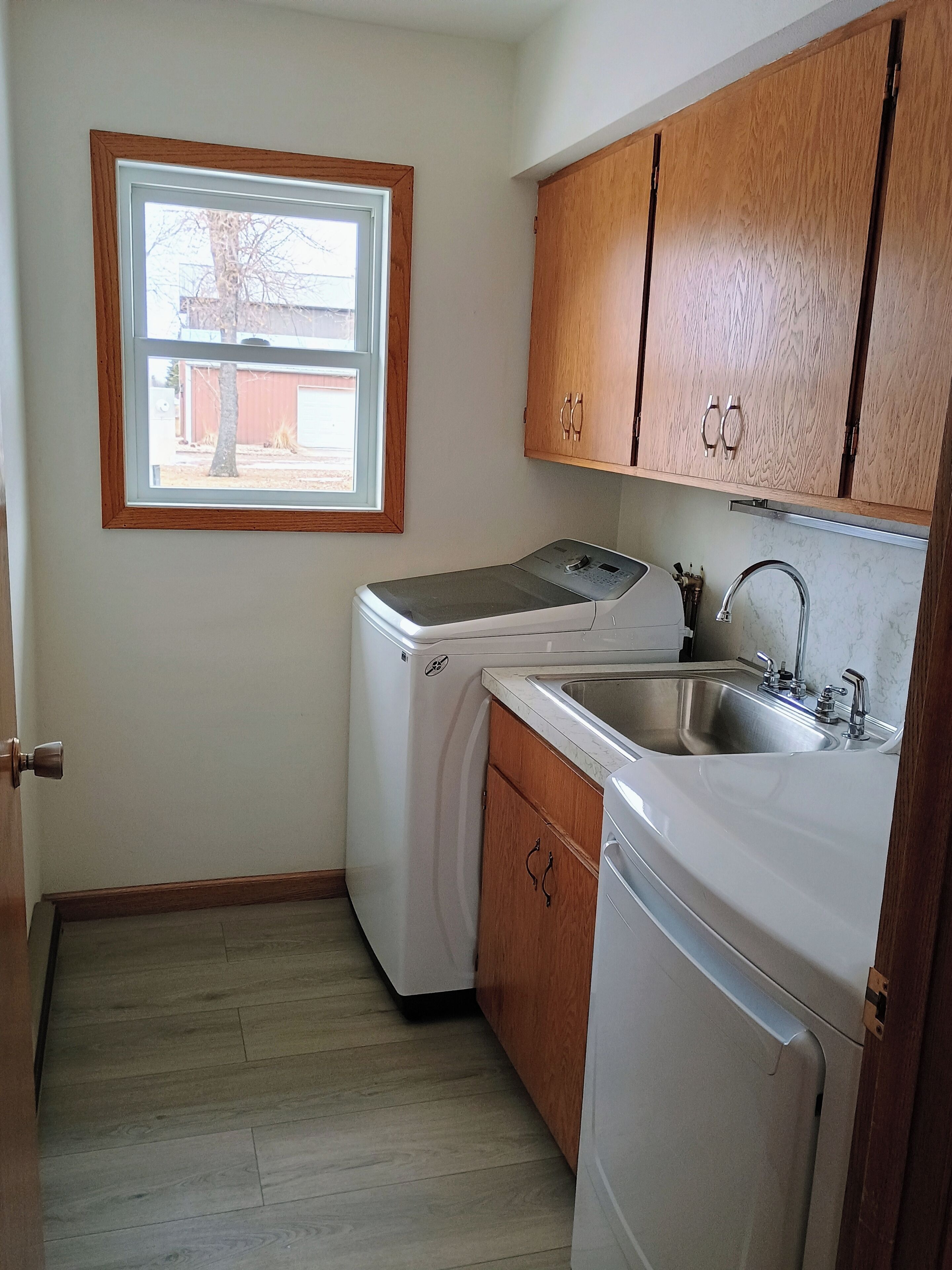 A compact kitchen with a washing machine, a sink, wooden cabinets, and a window.