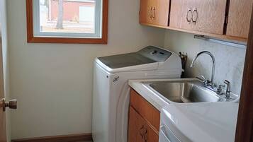 A compact kitchen with a washing machine, a sink, wooden cabinets, and a window.