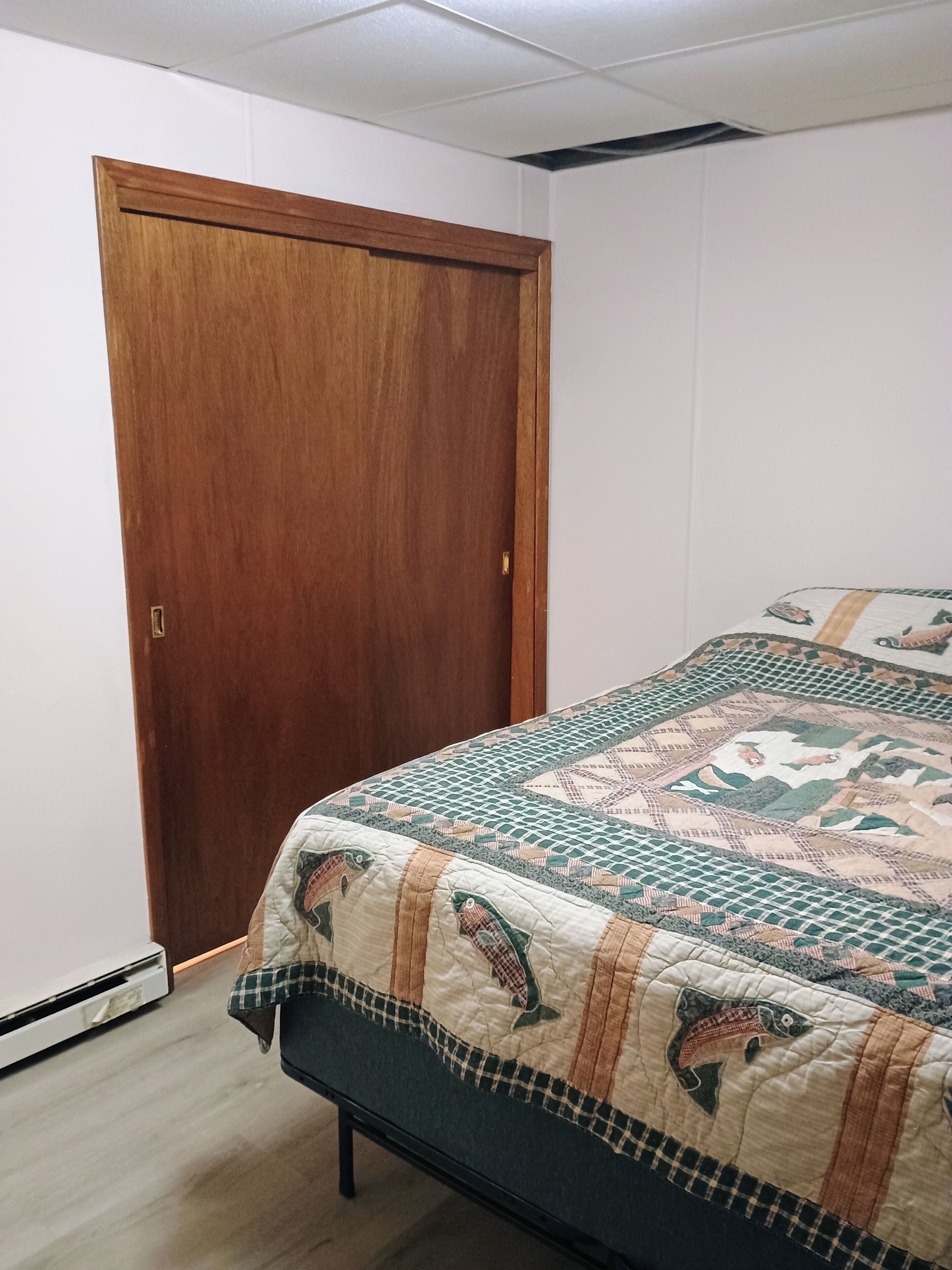 A bedroom with a wooden door, a bed with a quilt featuring fish patterns, and a white wall.