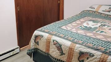 A bedroom with a wooden door, a bed with a quilt featuring fish patterns, and a white wall.