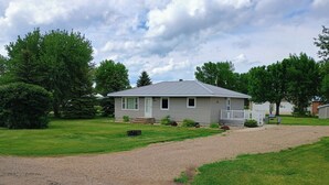 A single-story house with a gravel driveway, a front porch, and a well-maintained lawn. - Charming 3-bedroom Lake House with AC, WiFi in terrific Pick City (Pick City)
