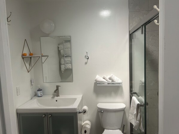 Un baño con lavamanos, espejo, inodoro y cabina de ducha de vidrio.