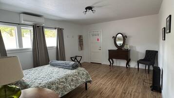 A bedroom with a bed, a table, a chair, a mirror, and a door.