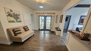 Un vaste espace de vie doté d’un plancher en bois, d’un canapé beige agrémenté de coussins à motifs, d’un coin repas avec une table et des chaises en bois, et d’une cuisine équipée d’un comptoir et d’un évier.