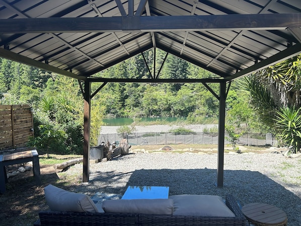 A covered outdoor seating area with a view of a river and greenery.
