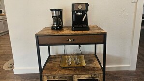 Un coin café avec deux machines à café posées sur une table en bois, un tableau encadré accroché au mur et un meuble rustique en dessous.