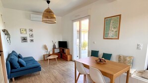 A spacious living area with a blue sofa, wooden dining table, and a television.