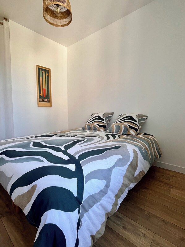 Un dormitorio con una cama, almohadas, una lámpara colgante y una obra de arte en la pared.