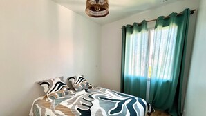 A bedroom with a bed, a hanging light fixture, and a window with curtains.