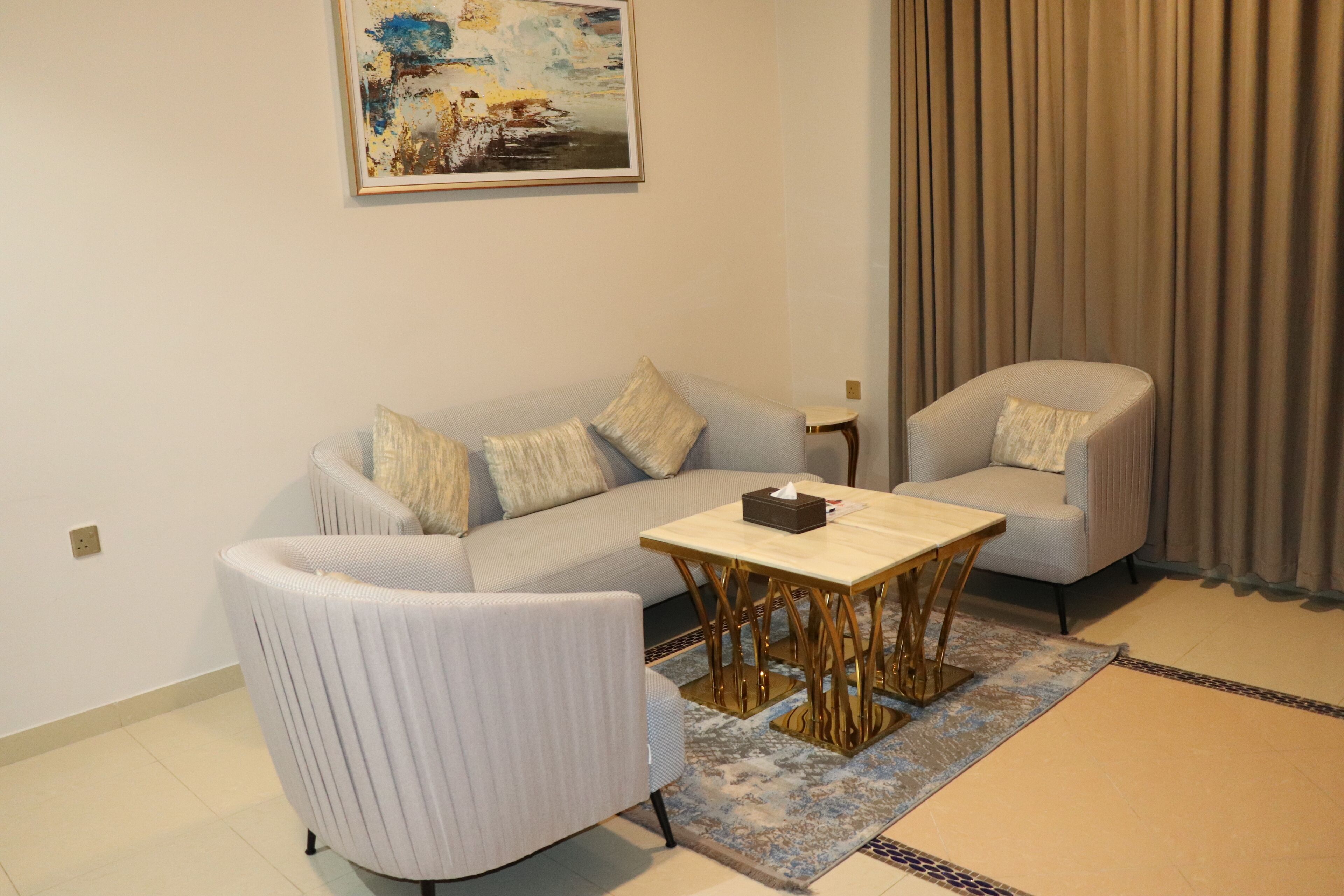 A modern living room with a sofa, armchairs, a coffee table, and a painting on the wall.
