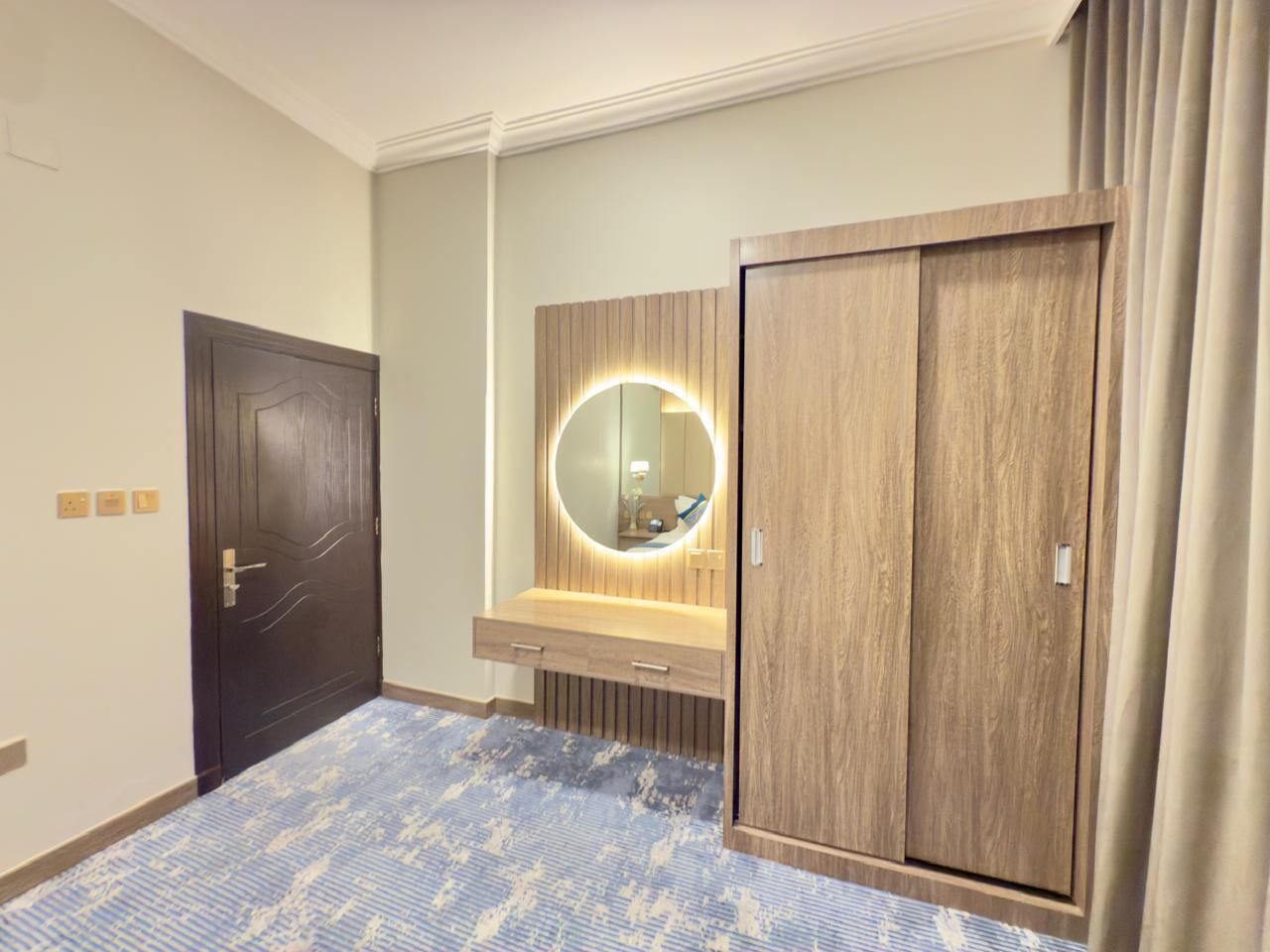 Une chambre d’hôtel avec une porte en bois sombre, une coiffeuse avec un miroir et une armoire en bois.