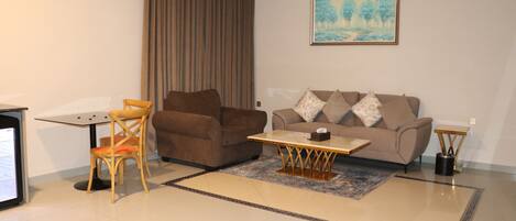 A living room with a brown sofa, a wooden chair, a small table, and a painting on the wall.