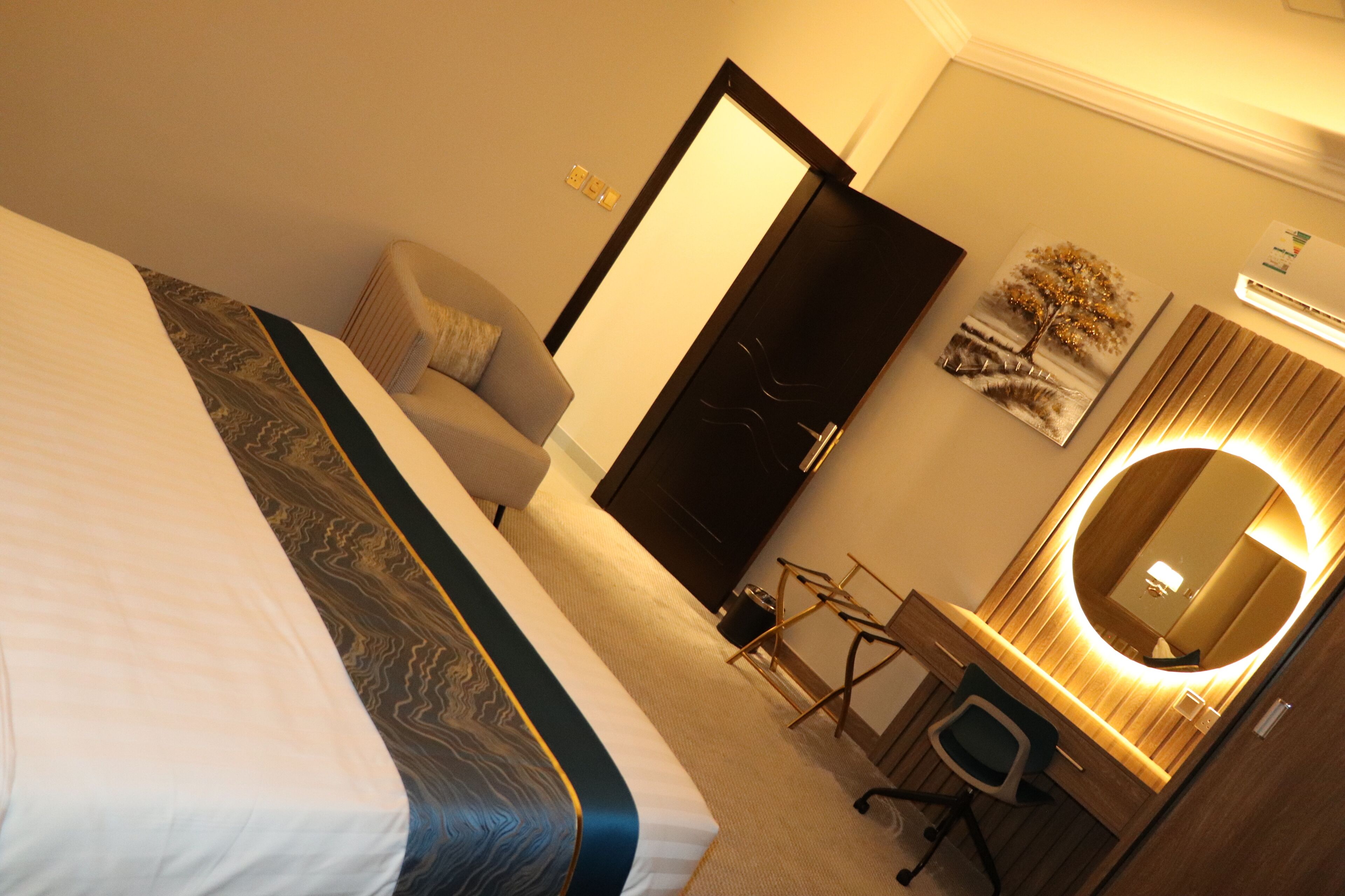 A hotel room with a bed, a desk, a chair, a mirror, and a door.