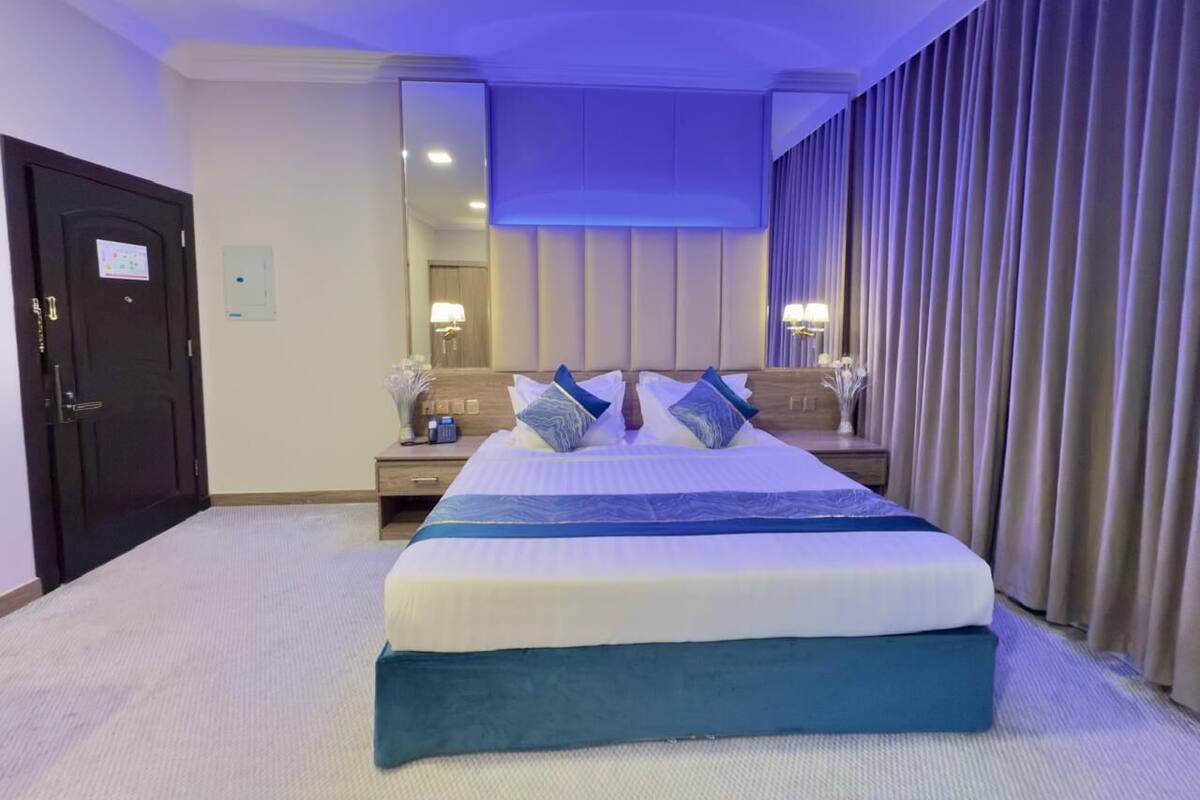 Une chambre d’hôtel avec un grand lit, une table de chevet, un miroir et une fenêtre avec des rideaux.