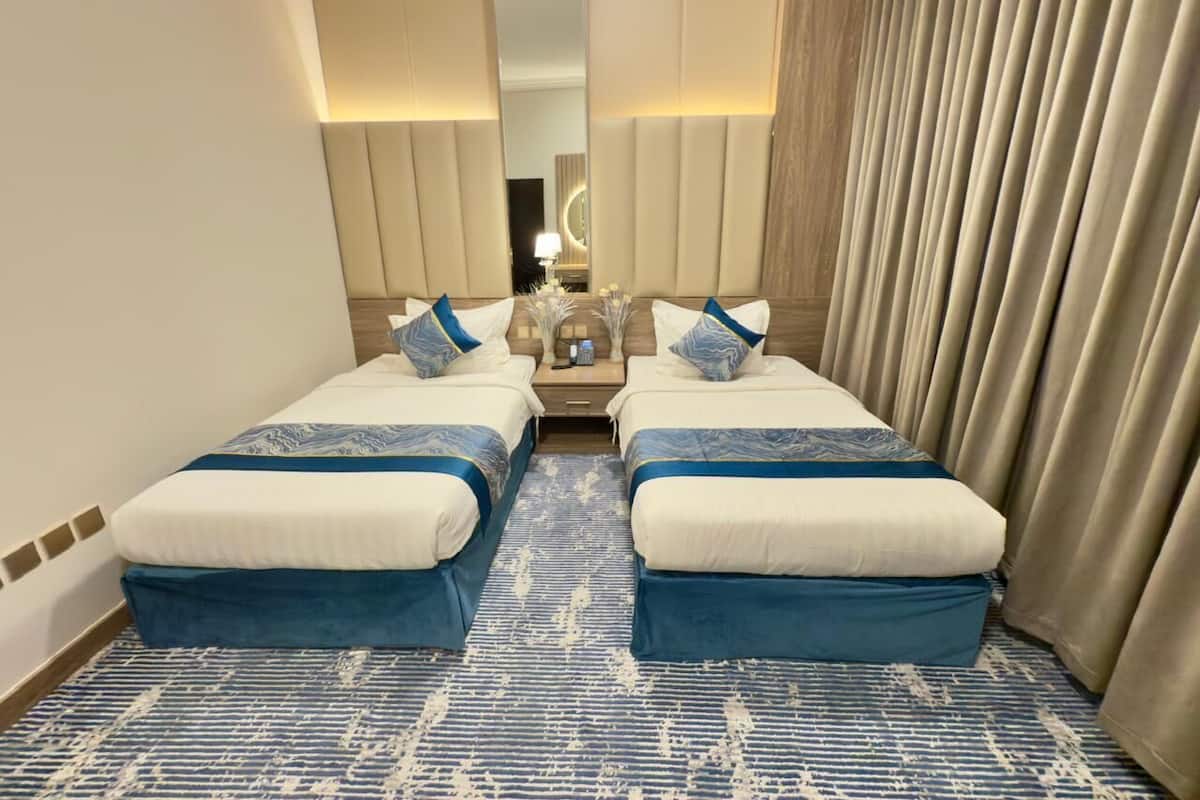 Une chambre d’hôtel avec deux lits, un grand miroir, une table de chevet et une moquette à motifs.