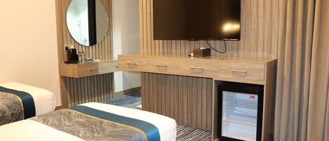 Ein Hotelzimmer mit zwei Betten, einem an einer Holzpaneele Wand montierten Fernseher, einer Minibar und einem kleinen Kühlschrank.