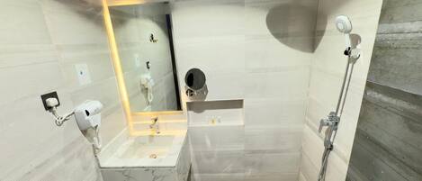 Un baño moderno con lavamanos de mármol, ducha de mano y espejo empotrado.