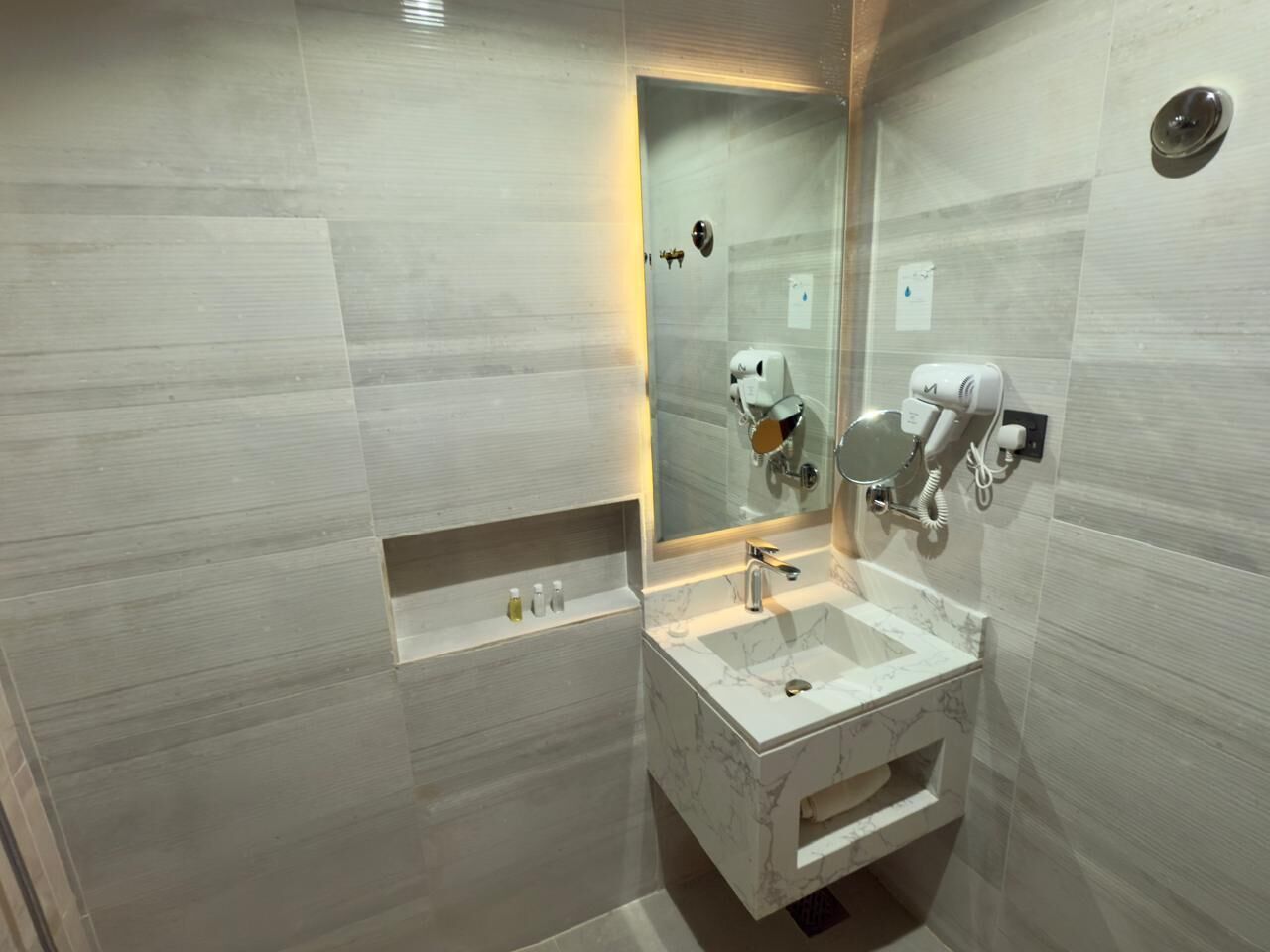 Un baño moderno con un lavamanos de mármol, un cabezal de ducha de mano y un secador de pelo incorporado.