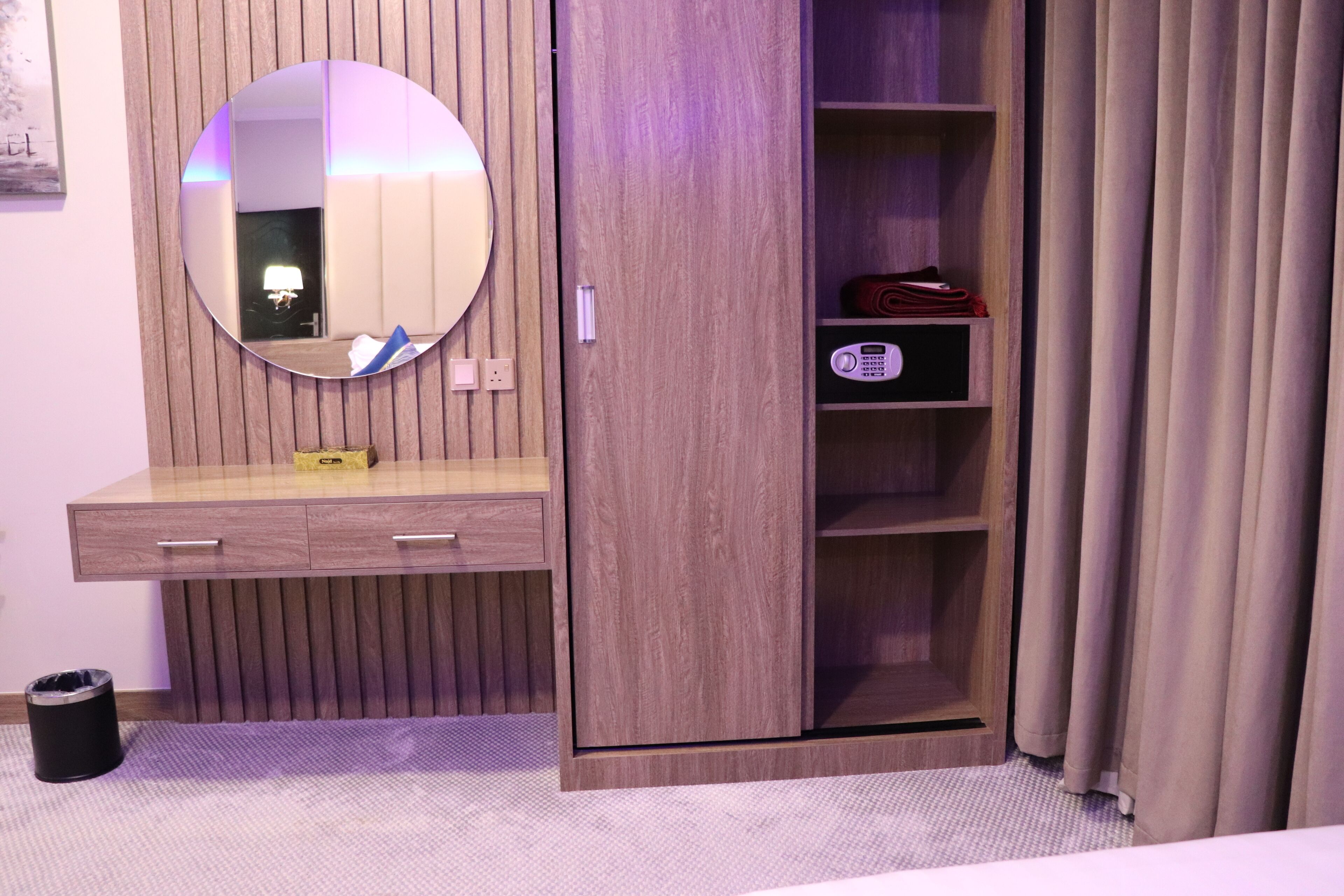 A bedroom with a wooden wardrobe, a mirror, a bedside table, and a bed.