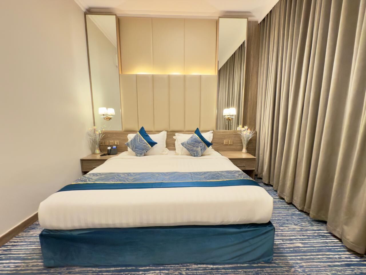 A hotel room with a large bed, a nightstand, a mirror, and a window with curtains.