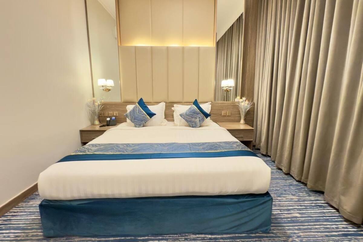 Une chambre d’hôtel avec un grand lit, une table de chevet, un miroir et une fenêtre avec des rideaux.