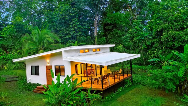 A modern house with a wooden deck, surrounded by lush greenery.