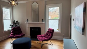 Un salon moderne avec une cheminée, deux fauteuils violets, un pouf bleu et un grand miroir au-dessus de la cheminée.